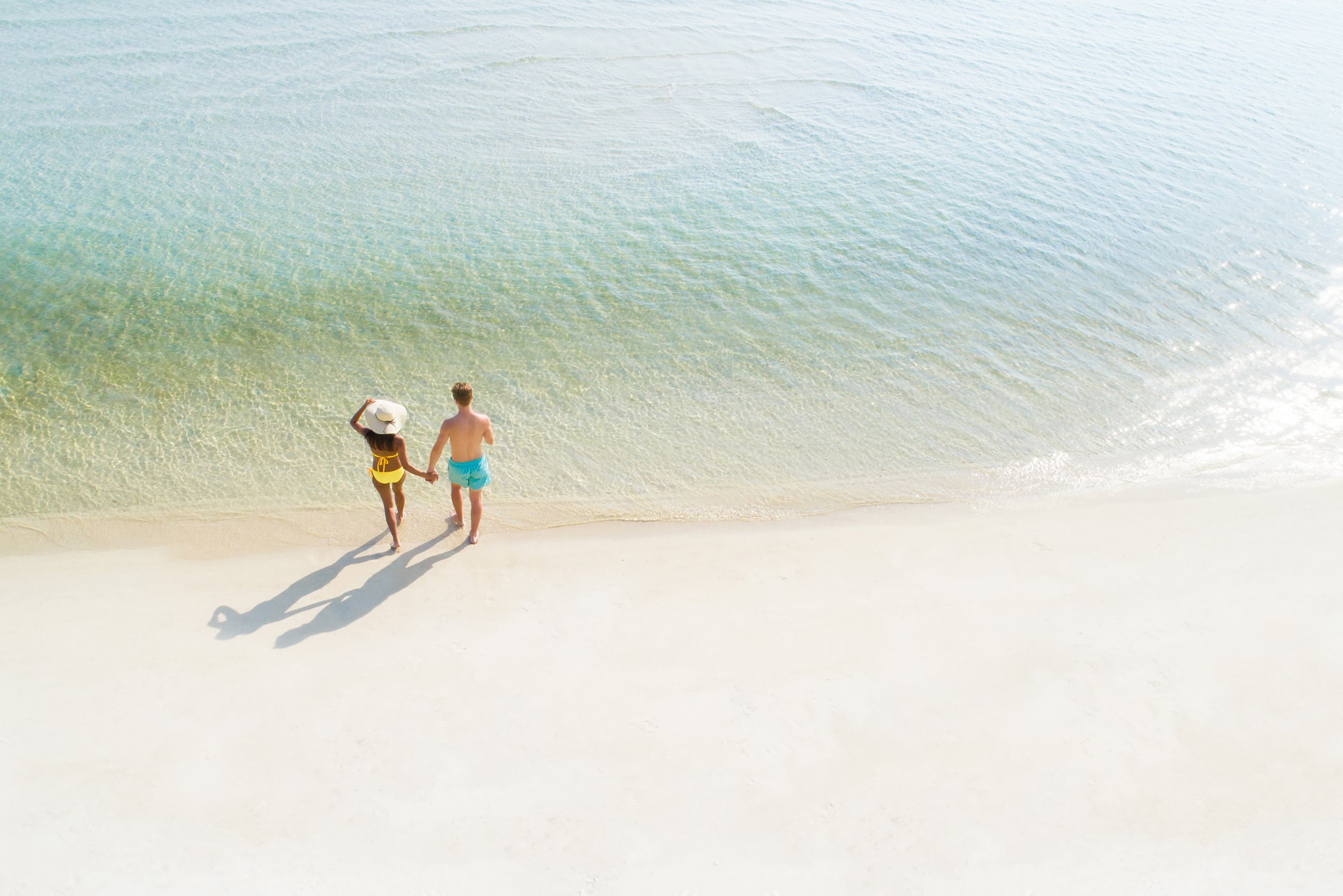 Honeymoon couple holding hand walking on beautiful white sand beach in summer